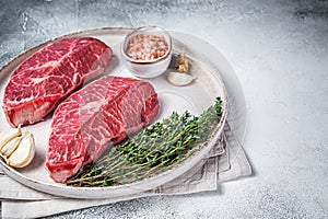 Raw Oyster Top Blade or flat iron roast beef meat steaks on a plate with herbs. White background. Top View. Copy space