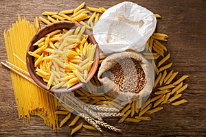 Raw pasta with flour, wheat ears and grains, top view