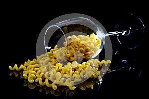 raw pasta in glass jar, wine glass. in bucket. raw pasta on black background. front view raw pasta, dropped from hand, place for