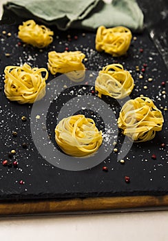 Raw pasta nests with spices and ground cheese on black marble table