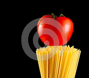 Raw pasta spaghetti with tomato on top on black background with space for text