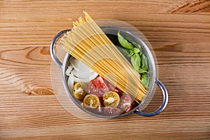 Raw pasta, tomato, basil and onion in pot on wooden background