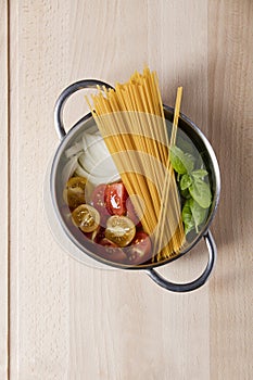 Raw pasta, tomato, basil and onion in pot on wooden background