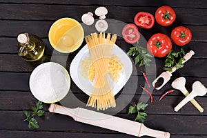 Raw pasta, tomatoes,mushrooms, flour and egg on black wooden table background