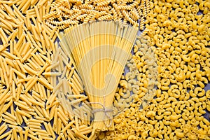 Raw pasta various kinds of uncooked pasta macaroni spaghetti and noodles on background - top view, Italian food culinary concept,