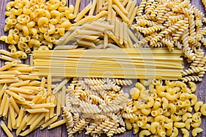 Raw pasta various kinds of uncooked pasta macaroni spaghetti and noodles on wooden - top view, Italian food culinary concept,