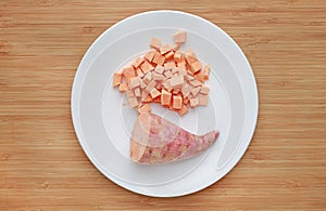 Raw peeled and chopped sweet potatoes in white plate on wood board background