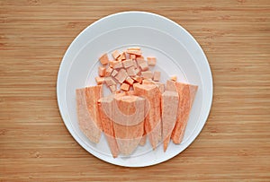 Raw peeled and chopped sweet potatoes in white plate on wood board background