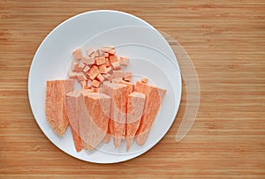 Raw peeled and chopped sweet potatoes in white plate on wood board background with copy space