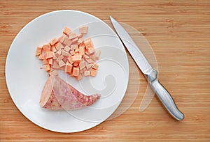 Raw peeled and chopped sweet potatoes in white plate on wood board background with sharp knife