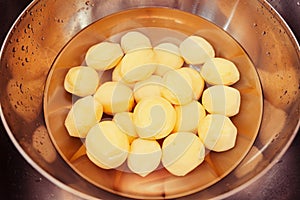 Raw, peeled potatoes submerged in water  in chrome bowl