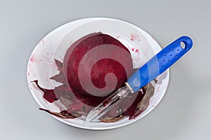 Raw peeled red beetroot and peeler among peelings in bowl photo