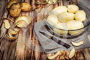 Raw peeled sliced potato, pile of potatoes and knife on rustic wooden table