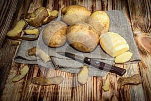 Raw peeled sliced potato, pile of potatoes and knife on rustic wooden table