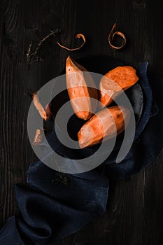 Raw peeled sweet potatoes on the wooden black table top view