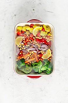 Raw peppers, potatoes, broccoli, chickpeas and onions with oil and spices in a baking dish.