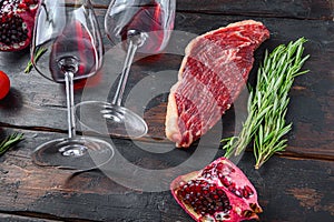 Raw picanha beef steak with rosemary, spicy chili oil, pomegranate and glass of red wine, on old dark wooden table side view,