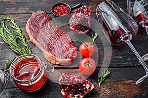 Raw picanha beef steak with rosemary, spicy chili oil, pomegranate and glass of red wine, on old dark wooden table side view,