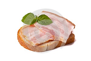 A raw piece of fresh bacon with a green basil leaf on a piece of white wheat bread isolated on a white background