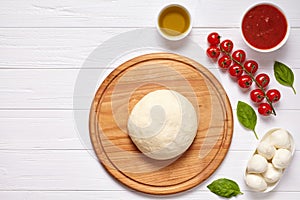 Raw pizza dough with baking ingredients on cutting board: dough, mozzarella, tomatoes sauce, basil, olive oil, cheese