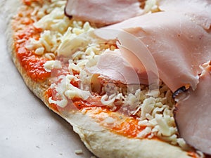 raw pizza dough with cheese, ham and sauce. clouseup