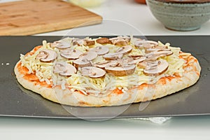 Raw pizza dough with tomato sauce, mozzarella, and Crimini mushroom slices.