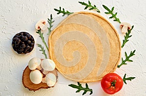 Raw pizza dough on the white background with free copy space. Dough with ingredients for veggie pizza: mushrooms, olives, rucola