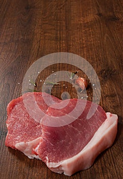 Raw pork chop steak and garlic, pepper on the brown wooden table background. rustic kitchen table with copy space. top view.