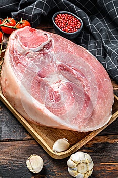 Raw pork ham cut on a wooden board. Leg meat. Dark background. Top view