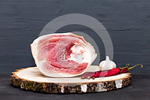 Raw pork leg on a cutting board next to pepper, garlic and spices