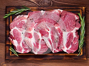 Raw Pork Loin chops on a cutting board with herbs rosemary on dark wooden background, top view