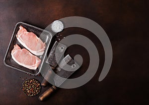 Raw pork loin chops in plastic tray with salt and pepper and vintage meat hatchets on rusty background.Space for text