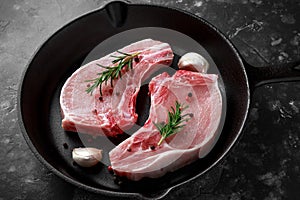 Raw Pork Loin chops in rustic skillet, pan with rosemary, garlic, pepper. top view. background