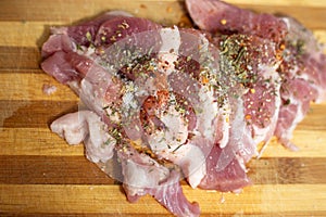 Raw pork meat on a cutting wooden board, sprinkled with seasonings, close-up