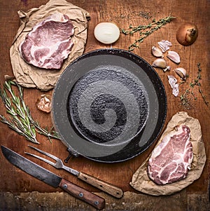 Raw pork meat with ingredients for cooking around cast-iron frying pan with knife for meat meat fork on rustic wooden backgrou