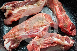 Raw pork ribs are fried in oil in a frying pan