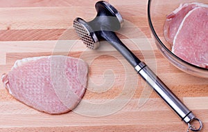 Raw pork schnitzel with meat tenderizer on wooden