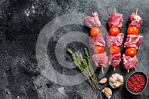 Raw pork shish kebab. BBQ meat with tomato and spices. Black background. Top view. Copy space