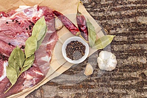 Raw pork shoulder with spices. Bay leaf, garlic, chili. On a wooden bark background