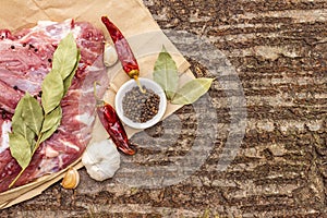 Raw pork shoulder with spices. Bay leaf, garlic, chili. On a wooden bark background