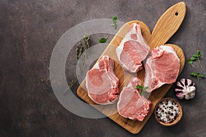 Raw pork slices on a cutting board with spices and herbs, dark rustic background. Top view, flat lay, copy space