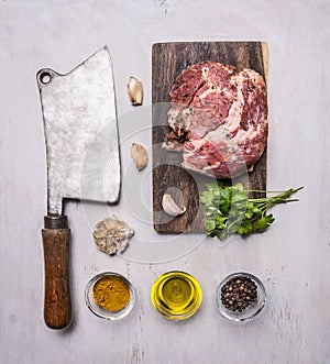 Raw pork steak on a cutting board and vintage meat cleaver with spices, garlic and herbs on wooden rustic background top view clos