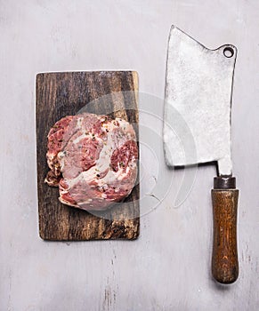 Raw pork steak on a cutting board and vintage meat cleaver on wooden rustic background top view close up