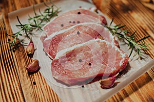 Raw pork steak on a dark wooden table with rosemary