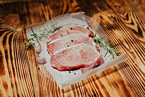 Raw pork steak on a dark wooden table with rosemary