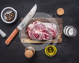 Raw pork steak with herbs, oil knife for meat on a cutting board on wooden rustic background top view close up