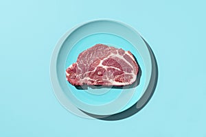 Raw pork steak on a plate, top view. Steak isolated on blue background