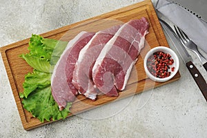 Raw pork steak - pork neck - with lettuce leaves on a wooden Board