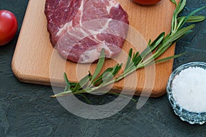 Raw pork steak, rosemary, tomatoes and salt on wooden cutting board, dark background, top view and side view