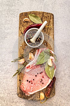 Raw pork steak with spices and dried herbs on vintage wooden board. Salt, garlic, hot pepper, rosemary, bay leaf with ceramic